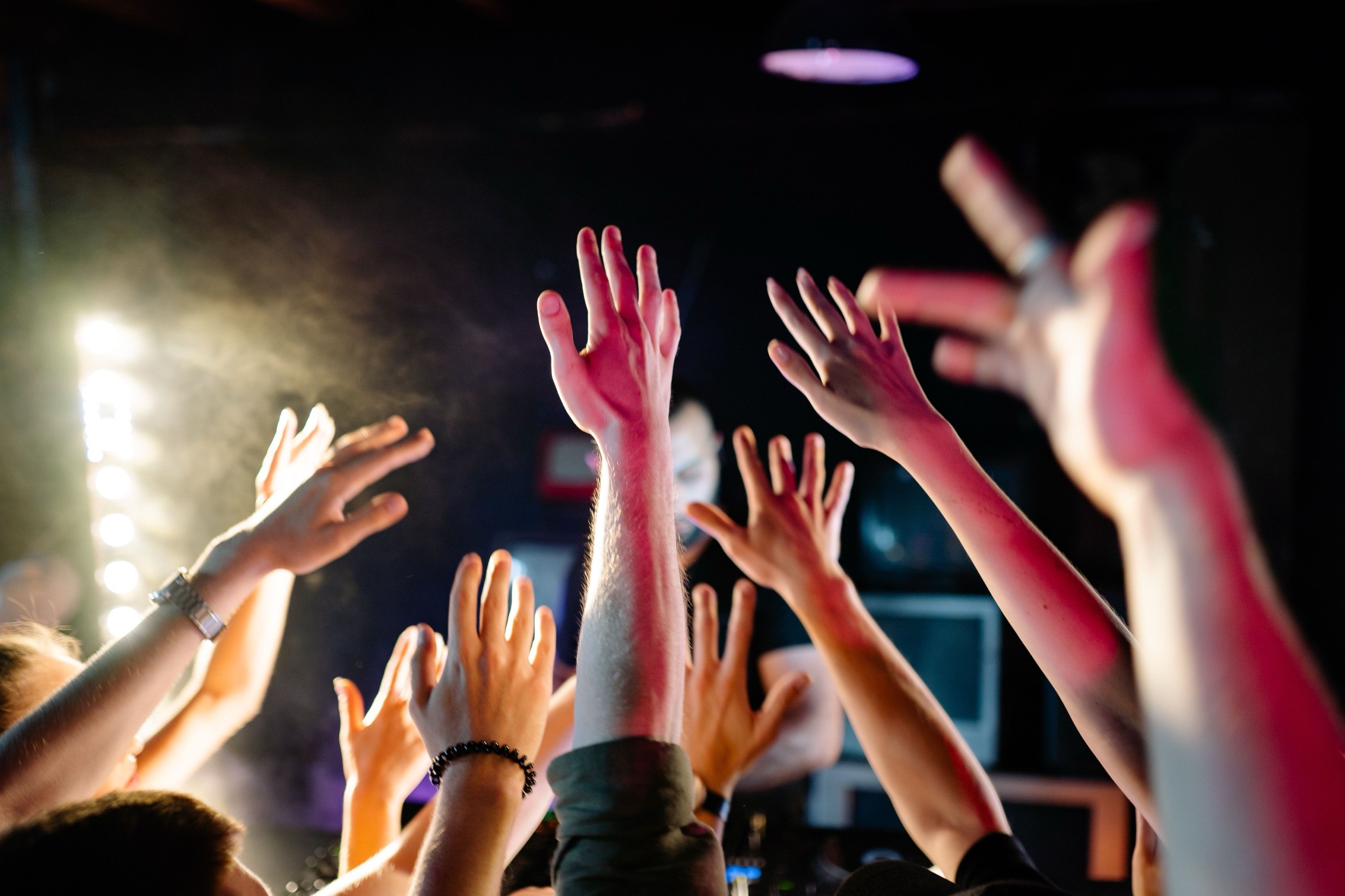 Crowd with hands raised in front of the DJ at a club night