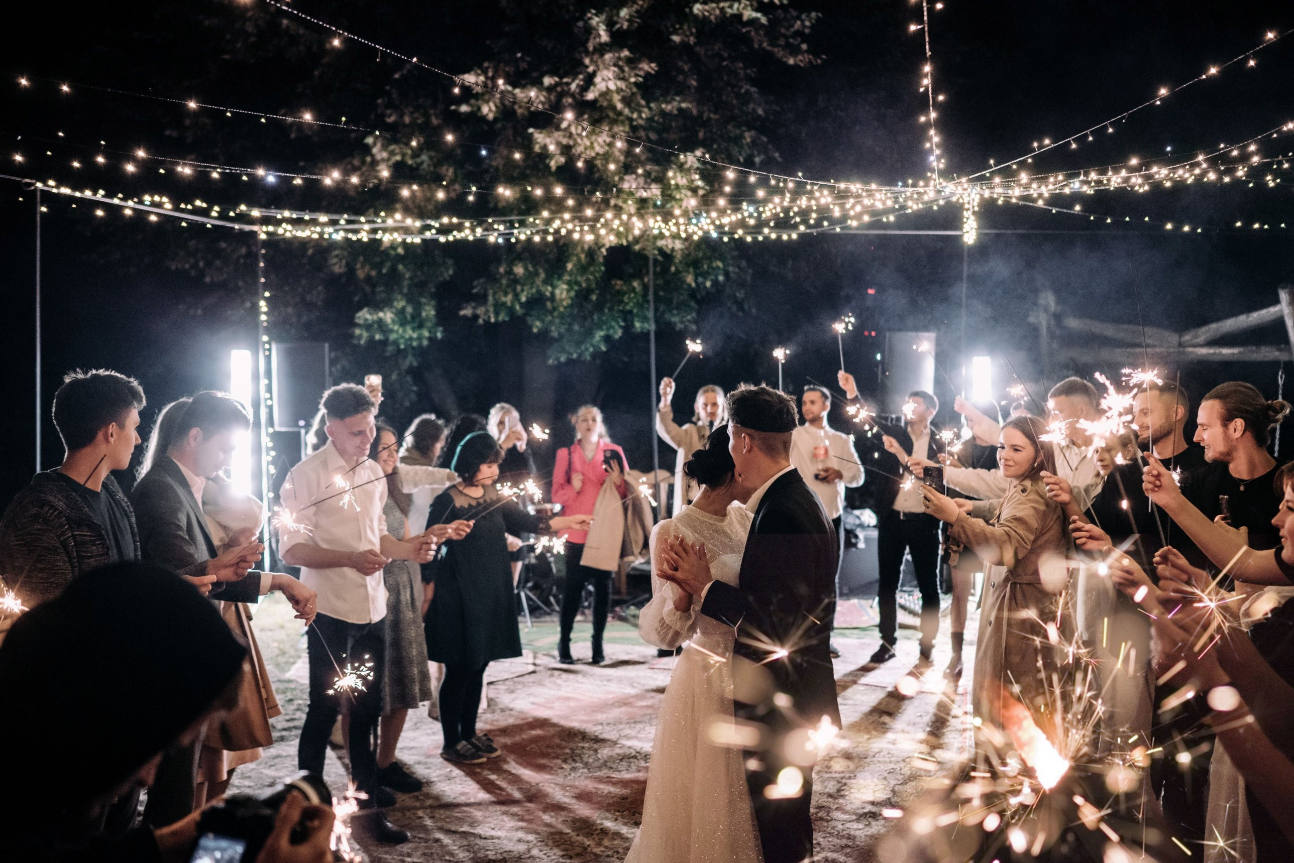 Guests holding sparklers around a couple dancing under string lights