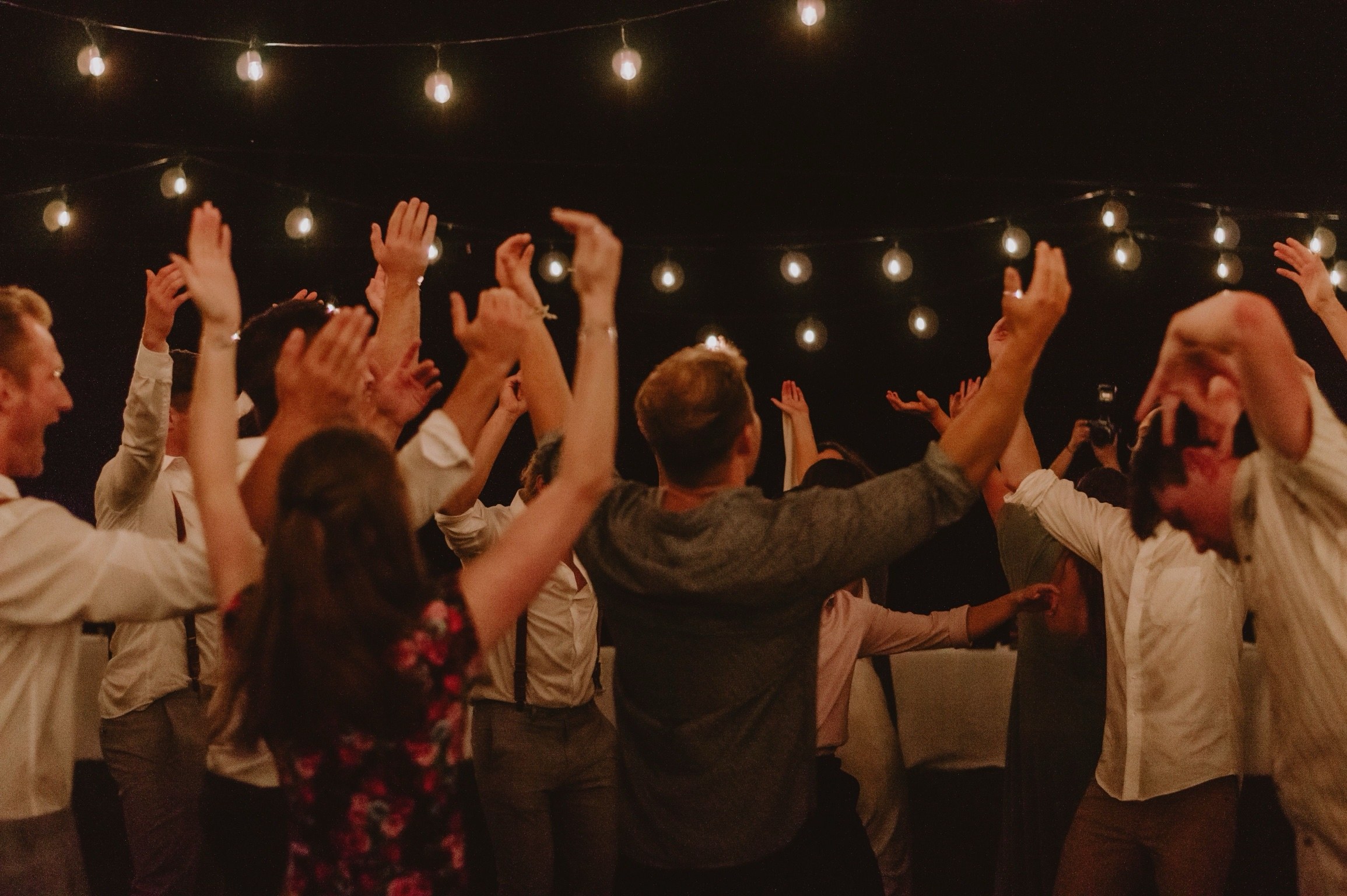 Wedding guests dancing with arms up under string lights