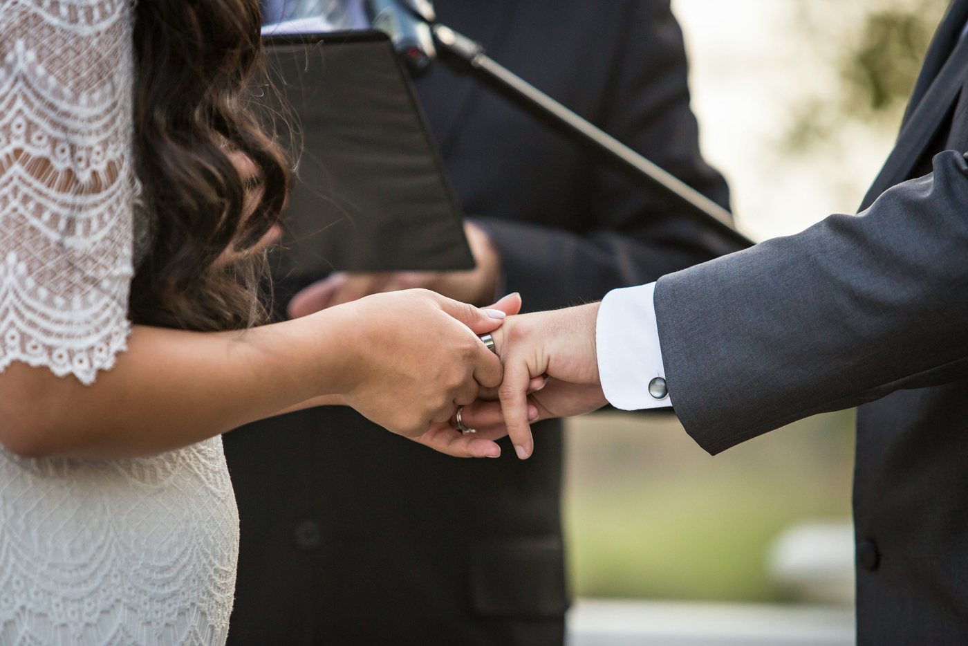 Couple exchanging rings in front of the officiant's microphone