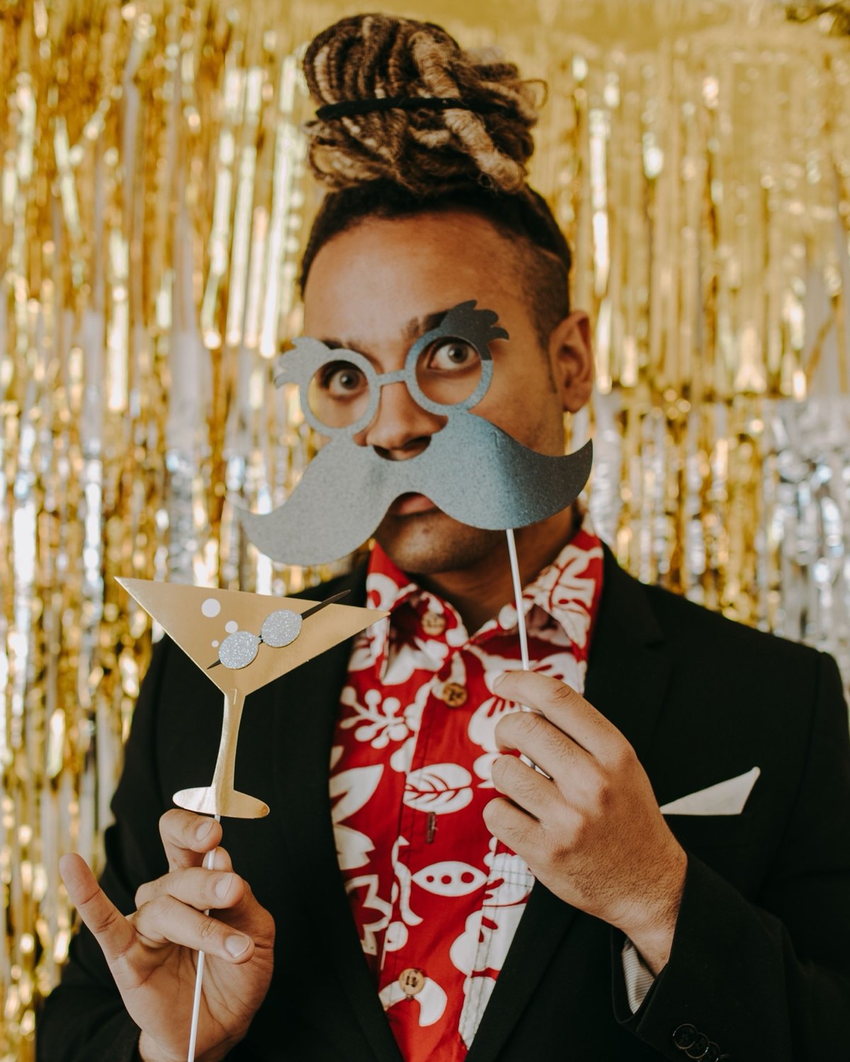 Guest posing with photo booth props in front of a gold streamer backdrop