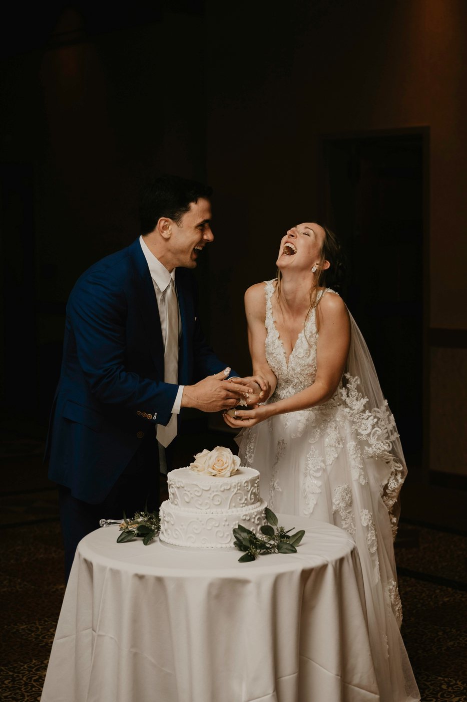 Couple laughing while cutting their wedding cake